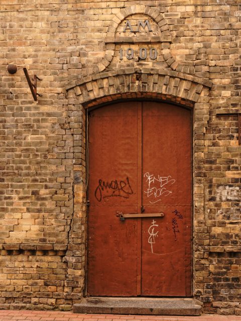 Bild: Tür an einem heute verlassenen Werkstattgebäude aus dem Jahre 1900 in der Alksnāja iela in der Altstadt von Riga. OLYMPUS OM-D E-M5 mit M.ZUIKO DIGITAL ED 12‑40mm 1:2.8. ISO 200 ¦ f/5,6 ¦ 25 mm ¦ 1/60 s ¦ kein Blitz. Klicken Sie auf das Bild um es zu vergrößern.