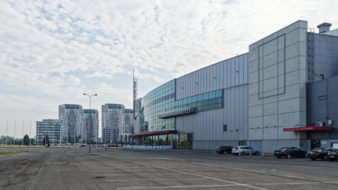 Bild: Die Mehrzweckhalle Arēna Rīga im Stadtteil Skanste von Rīga. Im Hintergrund sind die vier Hochhäuser "Skanstes virsotnes" zu sehen.