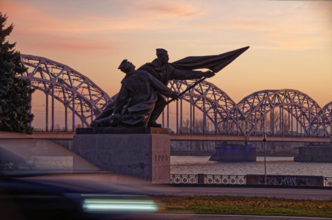 Bild: Sonnenuntergang an einem Novemberabend am Altstadtufer der Daugava in Rīga. Im Bild sind das Denkmal zu Ehren der Revolution von 1905 und die Eisenbahnbrücke zu sehen. Klicken Sie auf das Bild um es zu vergrößern.